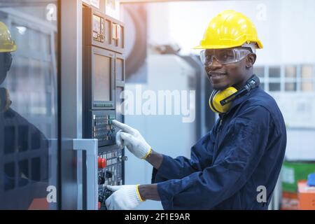 Schwarzer Mann, der bei programmierbaren Maschinen in der Fabrikindustrie arbeitet Stockfoto