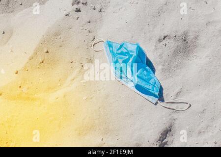 Gebrauchte weggeworfene medizinische Schutzmaske auf dem Strandsand. Meeresstrand Müll und Verschmutzung. Stockfoto