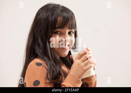 EIN JUNGES MÄDCHEN LÄCHELT MIT EINEM GLAS FRÖHLICH AN DIE KAMERA MILCH IN DER HAND Stockfoto