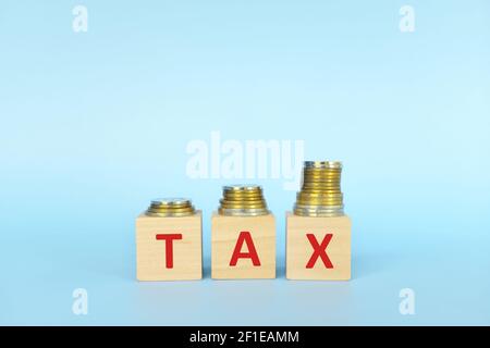 Steuerwort auf Holzblöcke in blauem Hintergrund mit zunehmendem Münzstapel. Konzept für steigende Steuern. Stockfoto