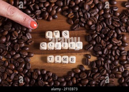 Frau Finger zeigt die Phrase seine Zeit Kaffee auf Holzwürfeln. Kaffeebohnen um sie auf einem Holztisch. Stockfoto