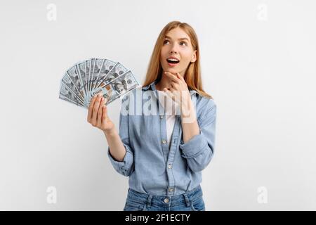 Junge glücklich denkende schöne Frau mit Haufen von Banknoten suchen Oben isoliert auf weißem Hintergrund Stockfoto