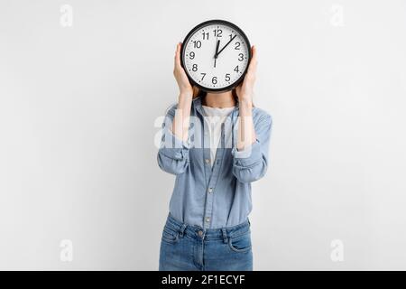 Junge Frau bedeckt ihr Gesicht mit rund Uhr isoliert auf Weißer Hintergrund Stockfoto