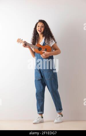EIN GLÜCKLICHER TEENAGER, DER DIE KAMERA ANSCHAUT UND UKULELE SPIELT