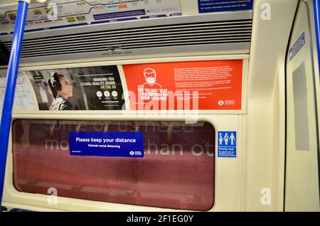 Passagiere und covid 19 Pandemie Gesicht Abdeckung und soziale Distanzierung Schilder auf die londoner U-Bahn-Züge 2021 Stockfoto