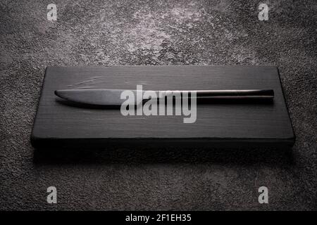 Ein schwarzes Tischmesser auf einem Holzpodium. Stilvolles minimalistisches Stillleben. Stockfoto