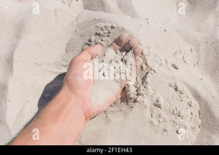Die Hand des Typen nimmt oder berührt den weißen Strandsand aus nächster Nähe. Stockfoto