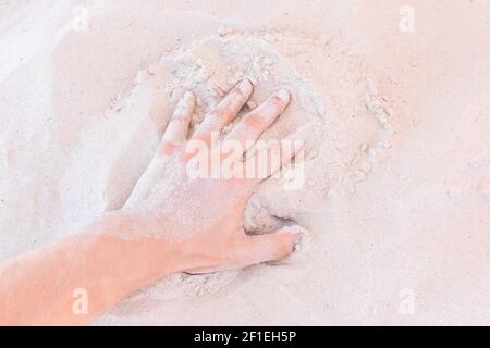 Die Hand des Typen nimmt oder berührt den weißen Strandsand aus nächster Nähe. Stockfoto