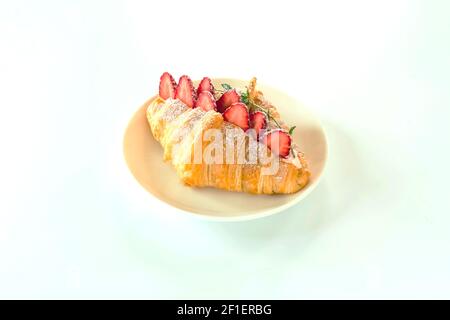 Frisch gebackene Croissants gefüllt mit frischen Erdbeeren auf weißem Teller. Croissant-Sandwich mit Erdbeeren, hausgemachtes Isolat mit weißem Hintergrund. Stockfoto