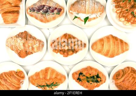 Draufsicht auf frisch gebackene leckere Croissants, verschiedene Arten und Geschmacksrichtungen auf weißem Teller, hausgemachte Isolate mit weißem Hintergrund. Französisches Gebäck. Tradi Stockfoto