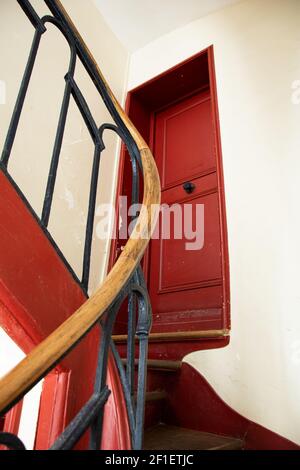 Typische schmale Wendeltreppe mit Geländer im alten Pariser Haus und roter flacher Tür. Selektiver Fokus. Stockfoto