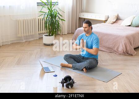 Foto eines Mannes im mittleren Alter während des Online-Dampfens. Meditationspraxis - Gebet Pose vor dem Laptop-Monitor zu Hause. Stockfoto