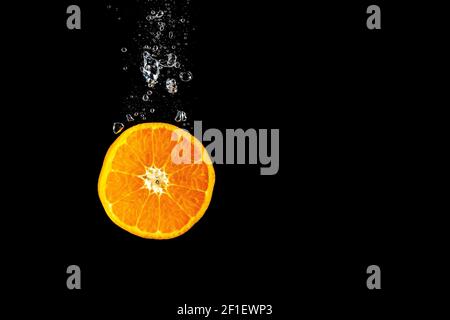 Orange, die mit Luftblasen ins Wasser fällt. Foto auf schwarzem Hintergrund. High-Speed-Fotografie. Stockfoto