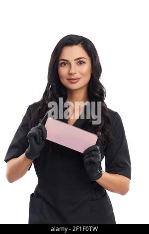 Frontansicht der attraktiven jungen Kosmetikerin in medizinischen Uniform und schwarzen Handschuhen mit rosa Kosmetik-Box. Professionelle Behandlung für Ihre Haut. Stockfoto