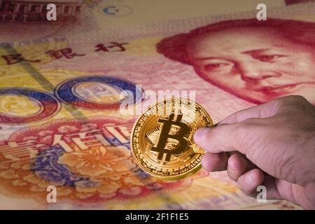 Hand hält eine Bitcoin und chinesische Yuan-Scheine in der Hintergrund Stockfoto