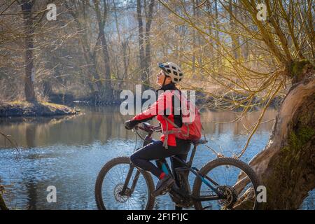 Eine nette und aktive ältere Frau klingelt an einem sonnigen Tag im Frühjahr an der Enz in Baden-württemberg, Deutschland, ihr elektrisches Mountainbike an Stockfoto