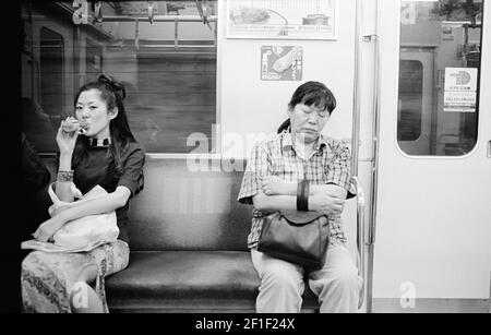 Tokio, Japan. Scene in der Tokyo Subway, mit einem jungen, schönen Mädchen, das trinkt, und einer reifen Frau, die schläft. Stockfoto