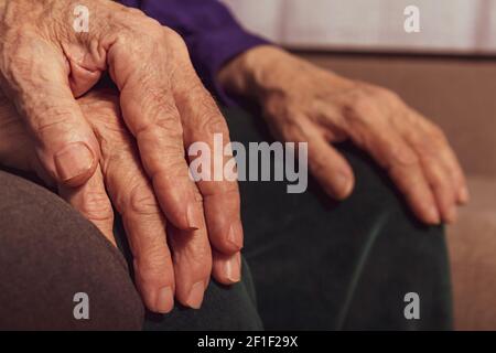 Ältere Ehepaare. Nahaufnahme gealterter Hände. Nicht erkennbare kaukasische Frauen- und Männerhände. Altes Ehepaar auf dem Sofa. Stockfoto