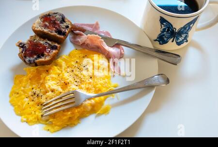 Rührei mit Schinken, geriebenem Käse, einem Blaubeer-Muffin und einem Becher schwarzen Kaffees Stockfoto