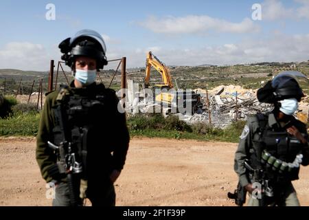 Hebron, Bani Naim Stadt in der Nähe der West Bank Stadt Hebron. März 2021, 8th. Ein israelischer Soldat und ein Mitglied der israelischen Grenzpolizei stehen Wache, als ein Bagger ein palästinensisches Haus im Bau zerstört, behauptet, dass es ohne Genehmigung gebaut wurde, in Bani Naim Stadt in der Nähe des Westjordanlandes Stadt Hebron, 8. März 2021. Kredit: Mamoun Wazwaz/Xinhua/Alamy Live Nachrichten Stockfoto