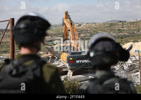 Hebron, Bani Naim Stadt in der Nähe der West Bank Stadt Hebron. März 2021, 8th. Ein israelischer Soldat und ein Mitglied der israelischen Grenzpolizei stehen Wache, als ein Bagger ein palästinensisches Haus im Bau zerstört, behauptet, dass es ohne Genehmigung gebaut wurde, in Bani Naim Stadt in der Nähe des Westjordanlandes Stadt Hebron, 8. März 2021. Kredit: Mamoun Wazwaz/Xinhua/Alamy Live Nachrichten Stockfoto
