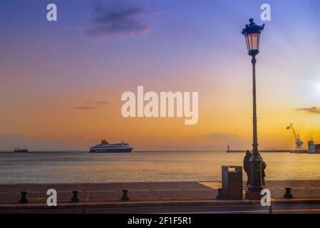 Thessaloniki, Griechenland Blue Star Mykonos Passagierschiff segelt zum Seehafen bei Sonnenuntergang und betritt ruhigen Seehafen mit hellenischer Flagge, die auf einem Kran verzichtet. Stockfoto