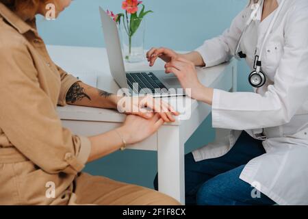 Patientin in der Arztpraxis, die darauf wartet, dass sie die Anamnese eines Patienten eingibt. Auf blauem Hintergrund. Sie trägt weiße Robe, Jeans und Stethoskop. Stockfoto
