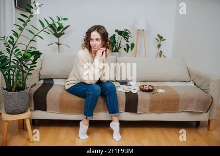 Nachdenklich junge Frau sitzt auf einer Couch im Komfort ihrer Wohnung neben Stickerment Werkzeuge und Materialien. Stockfoto