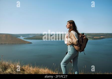 Schöne Frau mit Rucksack auf Berggipfel mit landschaftlich reizvoller Landschaft im Hintergrund stehen. Tolle Aussicht auf den breiten Dniester Fluss. Stockfoto