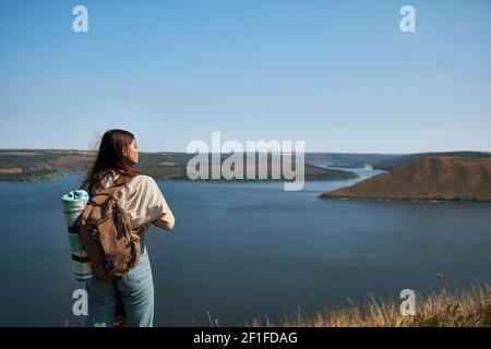 Rückansicht einer dunkelhaarigen Frau in legerem Outfit, die die wunderschöne Landschaft des Dniester Canyon bewundert. Weibliche Touristin mit Rucksack, die jeden Moment an Wochenenden im Freien genießt. Stockfoto