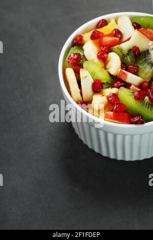 Obstsalat in einer weißen Tasse auf schwarzem Hintergrund, freier Platz für Text. Scheiben von frischen, saftigen und gesunden Früchten für eine gesunde Ernährung. Stockfoto