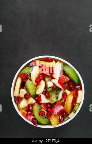 Frischer Obstsalatbecher aus saftigen Früchten auf schwarzem Hintergrund. Freier Speicherplatz für Text. Scheiben von frischen, saftigen und gesunden Früchten für eine gesunde Ernährung. Stockfoto