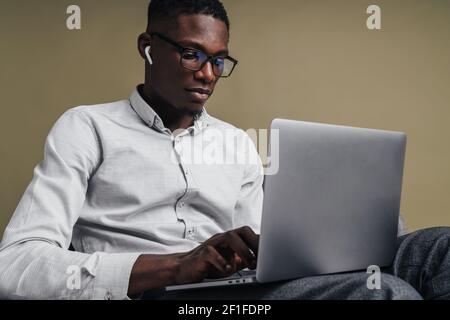 Selbstbewusster, gutaussehender Geschäftsmann, der auf einem Laptop sitzt, während er im Stuhl sitzt Isoliert auf grauem Hintergrund Stockfoto