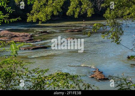 Blick von der Klippe auf den Chattahoochee Fluss in Georgien an einem Mann, der im seichten Wasser steht, fliegen Angeln in der Ferne auf einem hellen sonnigen Stockfoto