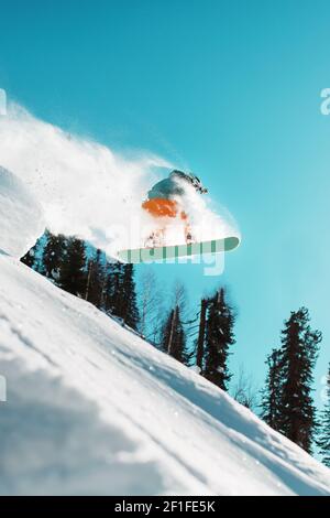 Ein Snowboarder springt von einem hohen schneebedeckten Sprungbrett in einem Wald gegen einen blauen Himmel. Extremsport Stockfoto