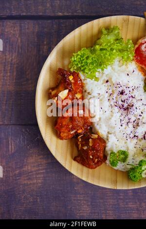 Hausgemachtes japanisches gegrilltes Hähnchengericht mit Gemüse und Reis, serviert auf einer Bambusplatte. Rustikale Holztisch Hintergrund. Stockfoto