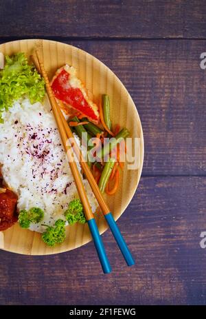 Hausgemachtes japanisches Reisgericht mit Gemüse und Huhn, serviert auf einem Bambusblech. Rustikale Holztisch Hintergrund. Stockfoto