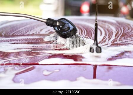 Pinsel hinterlässt Striche in weißem Shampoo und Schaum auf dem Dach Von rotem Auto gewaschen in Selbstbedienung Autowäsche Stockfoto