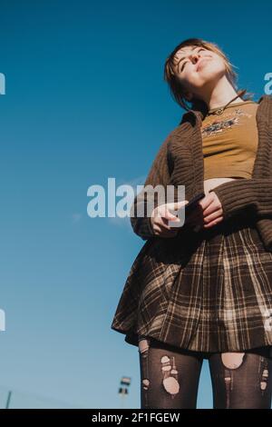 Porträt eines Skater Teenager-Mädchen in braun Tartan Rock Gegen einen blauen Himmel Stockfoto