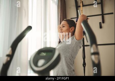 Portrait einer schönen jungen lateinamerikanischen Frau, die mit Hantel trainiert, während des Trainings im Heimstudio Trizeps pumpt Stockfoto