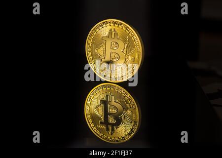 Einzelne Bitcoin-Münzen oder -Symbole stehen scharf im Fokus Eine reflektierende Oberfläche mit schwarzem Hintergrund Stockfoto