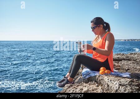 Lateinische Frau, mittleren Alters, ausruhen, Kraft zurückgewinnen, essen, Trinkwasser, nach einem Fitness-Studio-Sitzung, Kalorien zu verbrennen, fit zu halten, im Freien am Meer Stockfoto