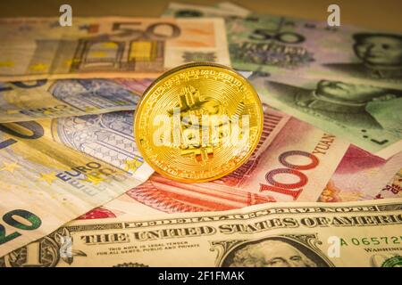 Goldene Bitcoin-Münze über Dollar-, Euro- und Yuan-Scheine Stockfoto