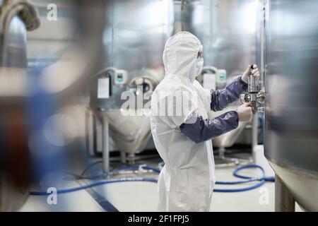 Seitenansicht Porträt eines männlichen Arbeiters, der Schutzanzug trägt, während er die Ausrüstung in einer modernen Chemiefabrik bediente, Kopierraum Stockfoto