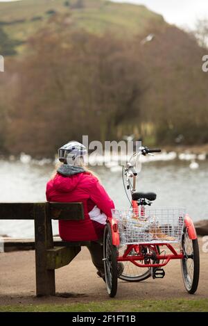 Edinburgh, Schottland, Großbritannien. März 2021, 8th. Eine Frau, die am St Margarets Loch (The Duck Pond) eine Pause macht, nachdem sie mit ihrem Dreirad um Holyrood Park gefahren ist, Edinburgh, 8. März 2021 Credit: Gayle McIntyre/Alamy Live News Stockfoto