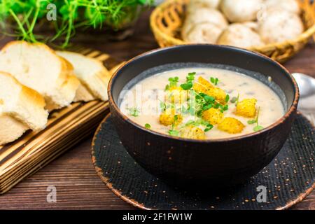 Eine Schüssel mit hausgemachter Pilzpüree-Suppe mit Kräutern und Brot auf einem Holztisch. Hausgemachte vegetarische Pilzsuppe mit Gemüse und Brot. Stockfoto