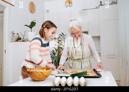 Ältere grauhaarige Frau macht mit ihrer Enkelin in der Küche Kekse. Stockfoto