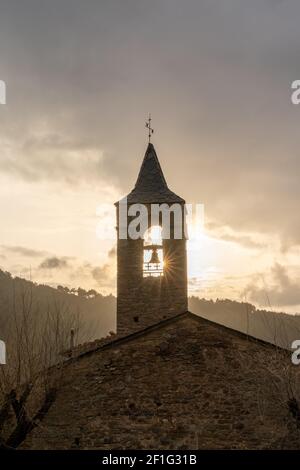 Eine massive Bergkirche aus Stein mit Kirchturm und Sonne Stern, der im Winter unter einem bewölkten Himmel durchscheint Abend Stockfoto