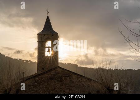 Eine massive Bergkirche aus Stein mit Kirchturm und Sonne Stern, der im Winter unter einem bewölkten Himmel durchscheint Abend Stockfoto