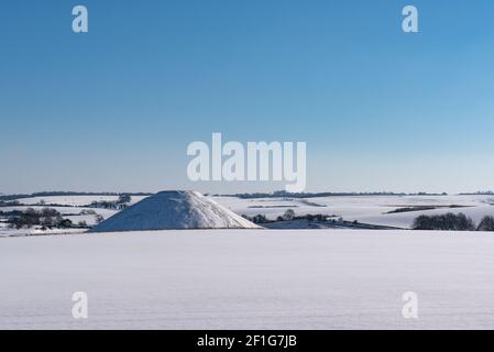 Die schneebedeckte uralte Wiltshire-Landschaft am Silbury Hill, Teil des Avebury-Weltkulturerbes. West Kennet Long Barrow ist auch sichtbar. Stockfoto